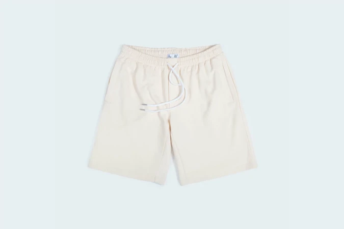 Studio shot of light beige shorts with drawstring, elastic waistband, and pockets, isolated on a light blue background.