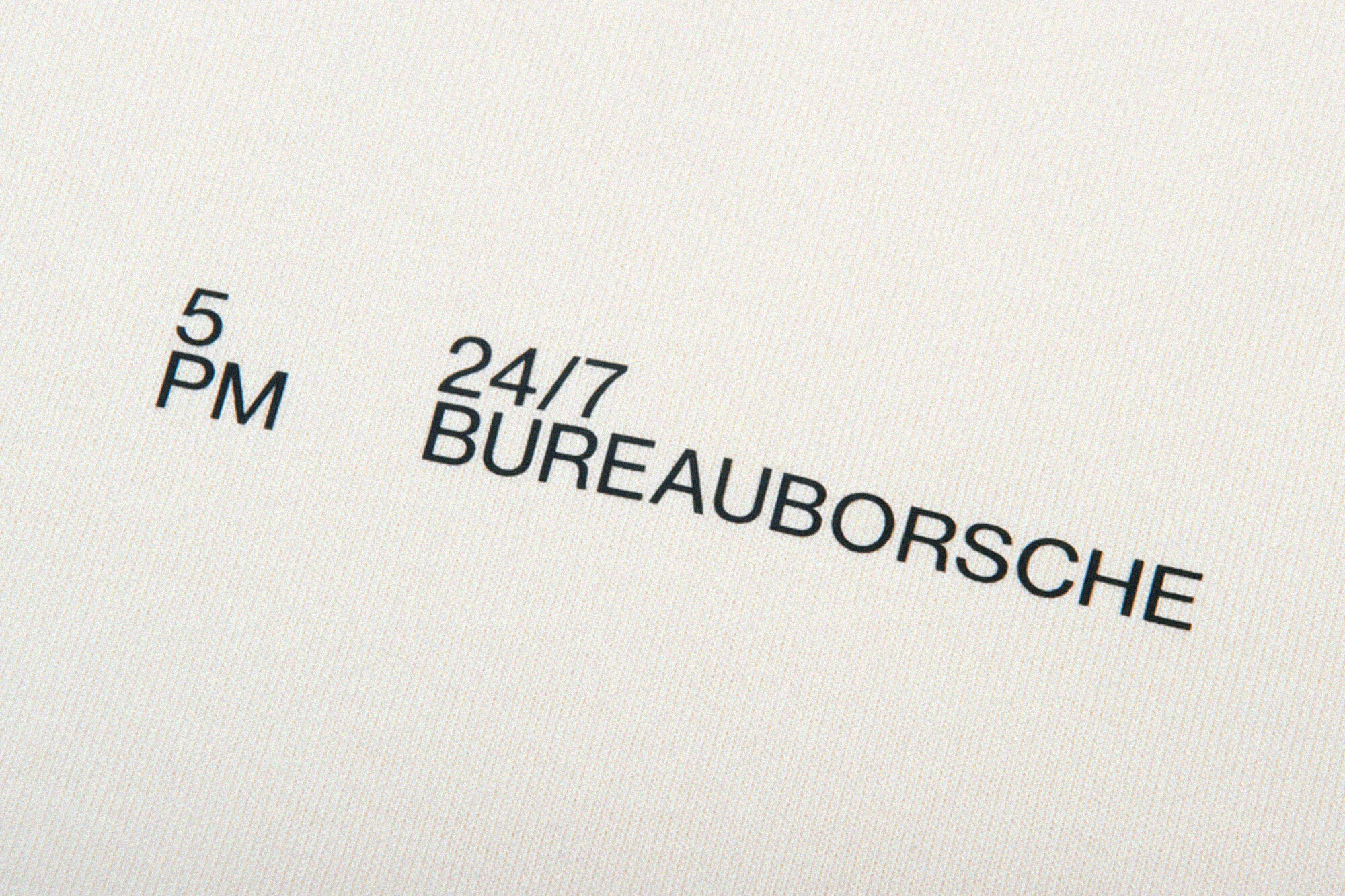 Abstract image of black text '5 PM' and '24/7 BUREAUBORSCHE' printed on an off-white surface in a close-up, studio shot.