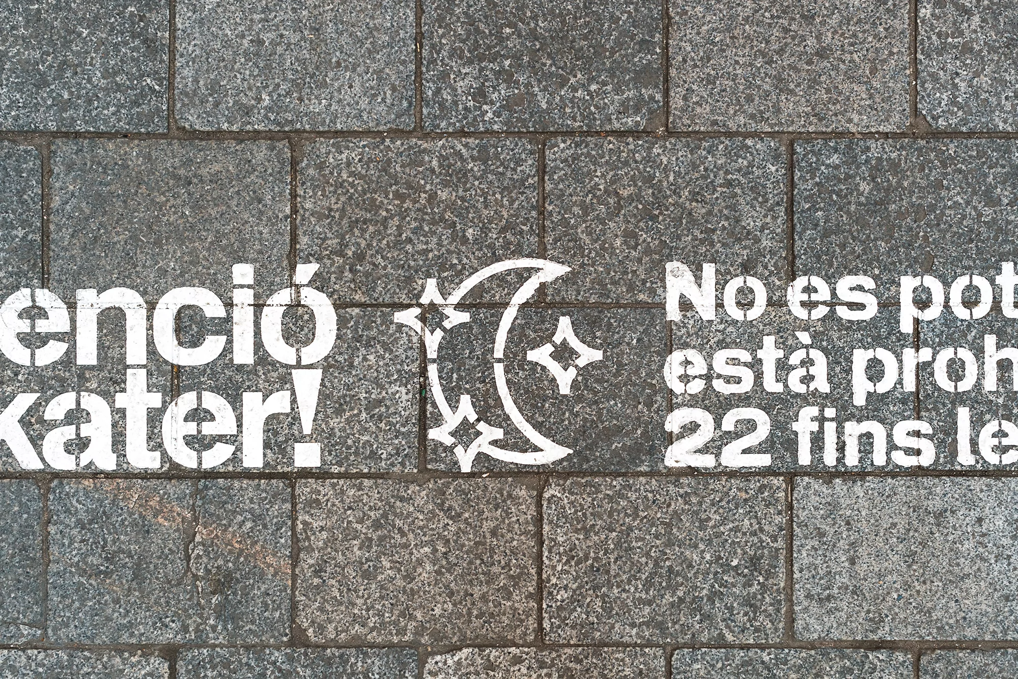 A gray stone sidewalk features white stenciled text and a moon and stars graphic, creating a textured and urban ground surface.