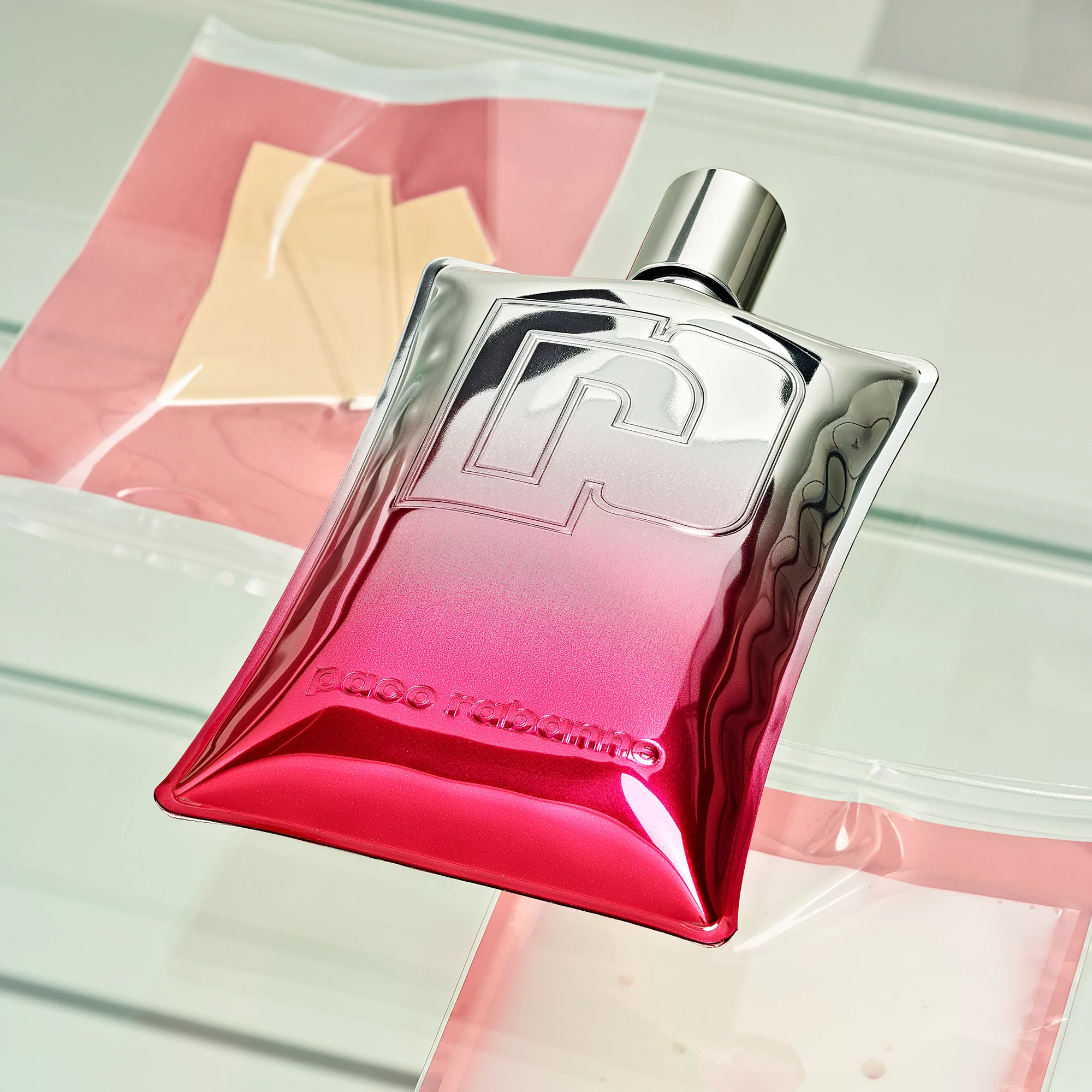 Chrome Paco Rabanne fragrance bottle with a pink gradient on a reflective shelf with pink translucent material. 