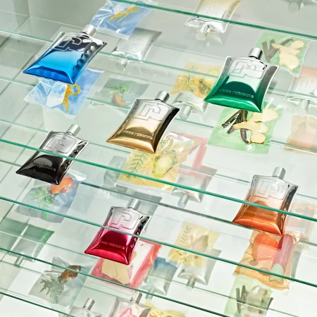 Still life shot of multiple colourful, metallic Paco Rabanne Phantom Parfum bottles displayed on glass shelves in a retail setting.