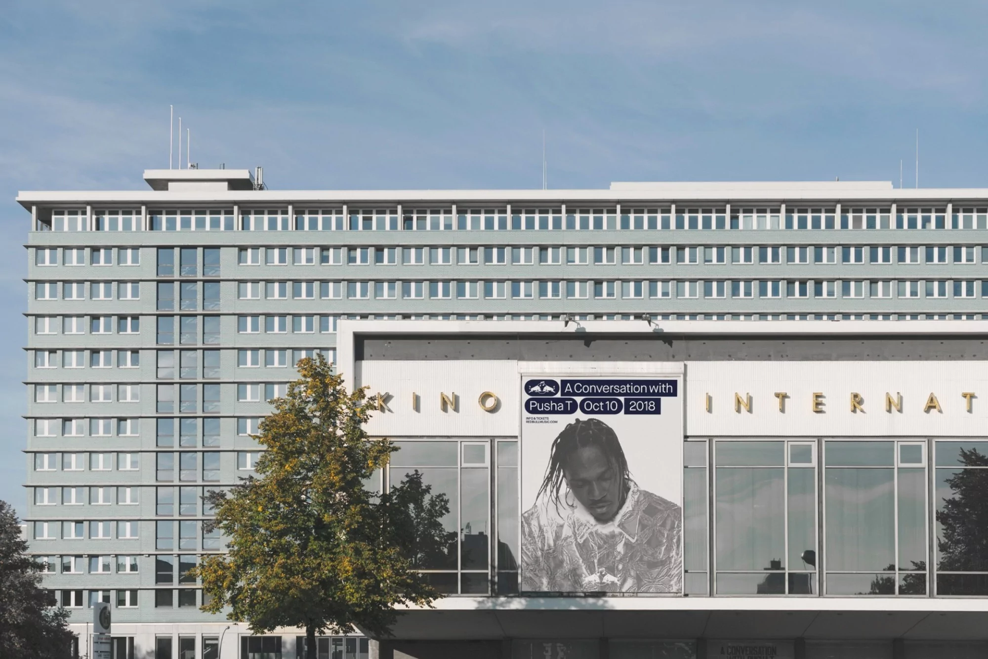 Building with large banner advertising 'A Conversation with Pusha T' event, featuring artist portrait and event details.