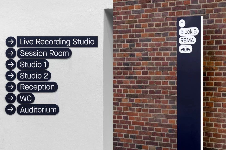 Indoor directional signs on a white wall pointing to spaces like the live recording studio, reception, and auditorium in a music complex.