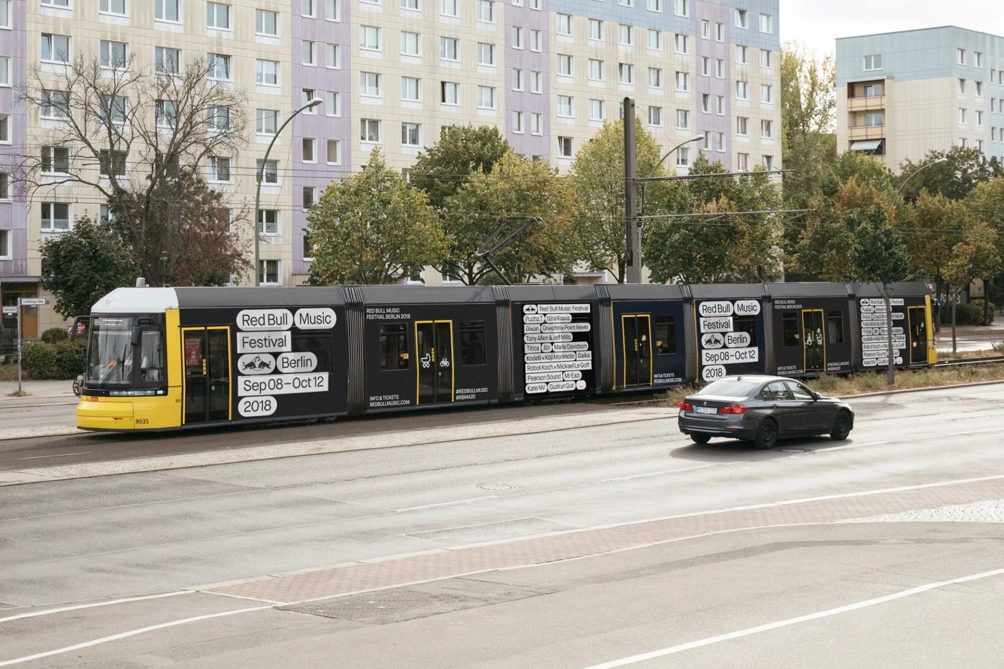 A yellow and black public transportation tram with Red Bull Music Festival Berlin advertisement, moving down a city street with a grey car.