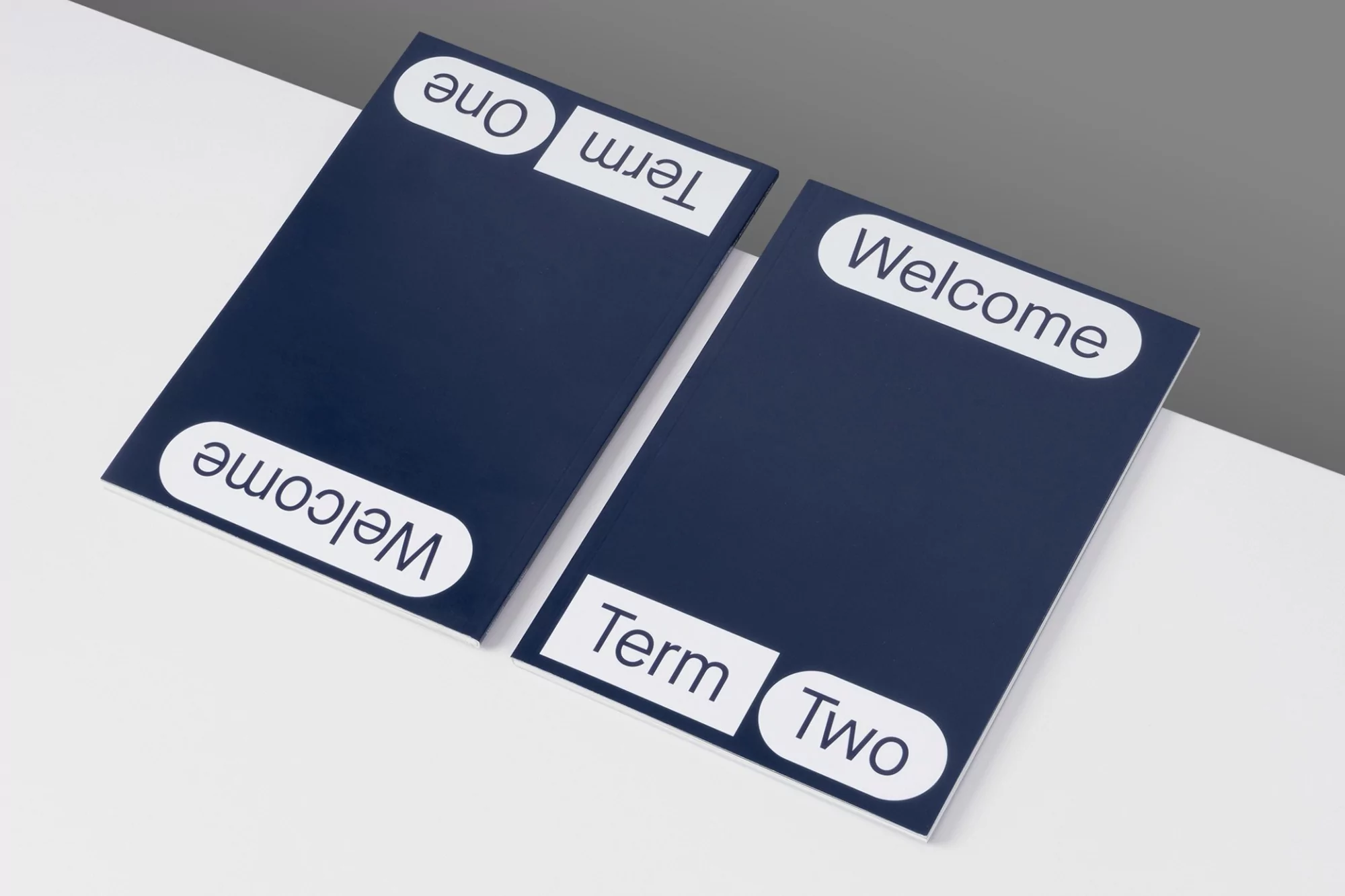 Two dark blue signs with white text on a white surface. The signs display 'Welcome', 'Term One', and 'Term Two' in a simple font.