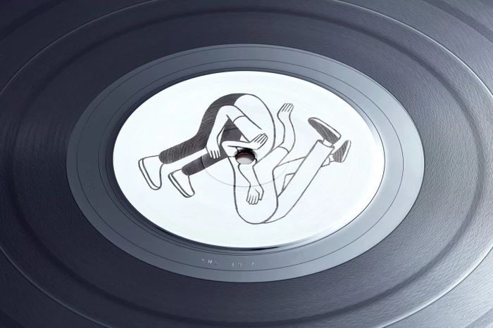 Close-up of a dark vinyl record with concentric grooves and a white center label featuring a black line illustration.