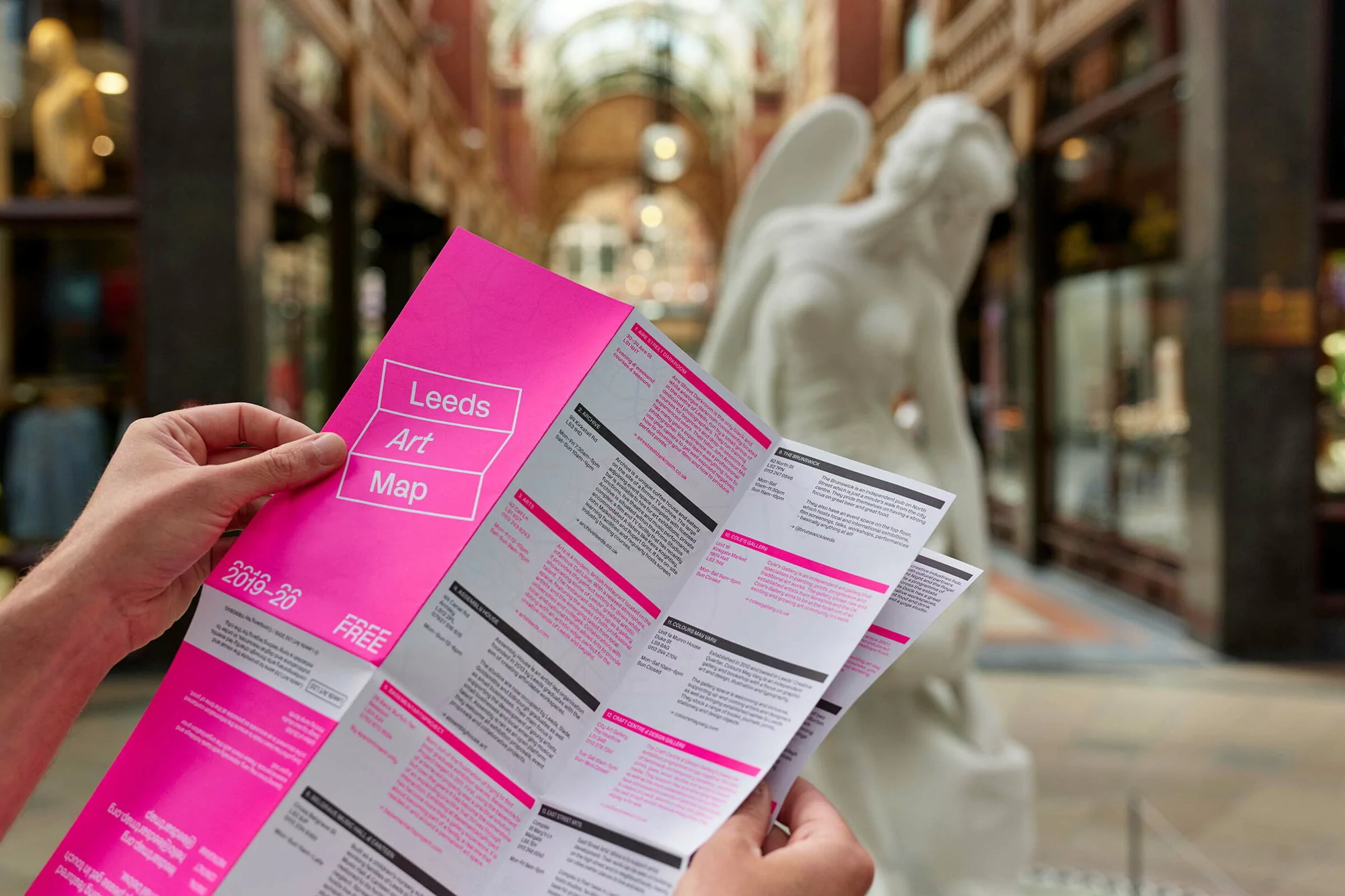 Person holding a pink art map in an indoor shopping arcade with a statue in the background, showcasing architecture and design.