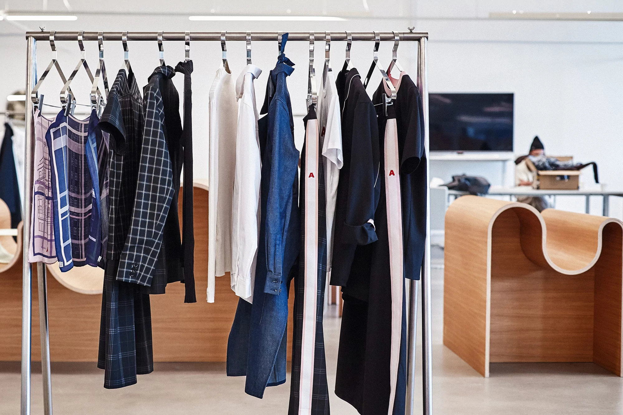 Rack of clothing with various garments including shirts, jackets, and dresses in a retail setting, modern minimalist style.