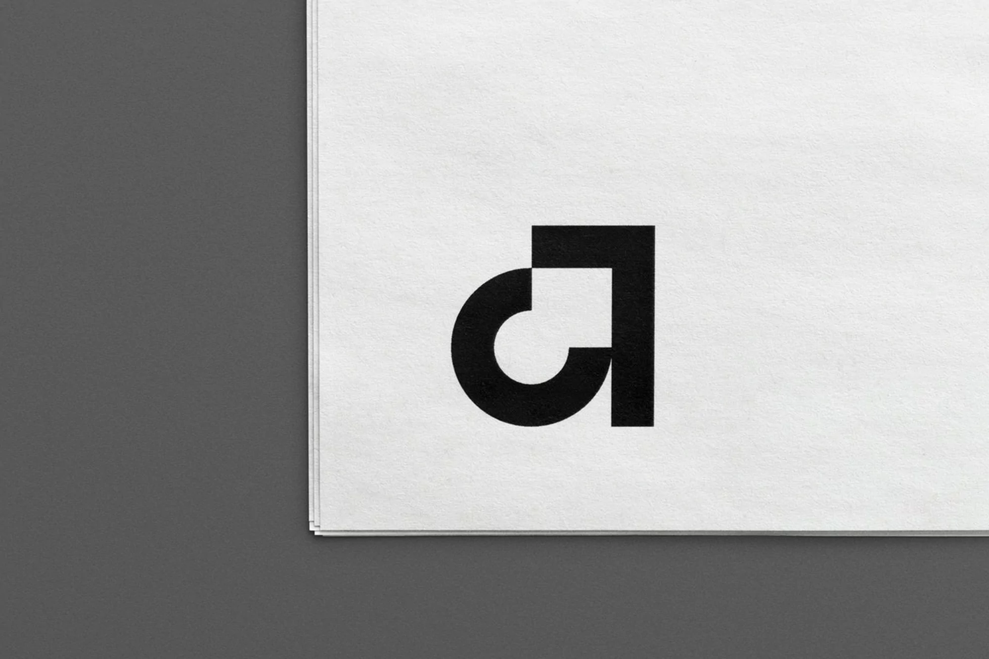 Black and white graphic design featuring a stylized, geometric logo on textured white paper with a gray background.