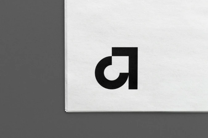 Black and white graphic design featuring a stylized, geometric logo on textured white paper with a gray background.