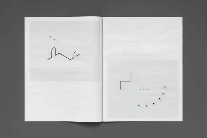 Open book displays minimalist line drawings and dot patterns on white pages, set against a solid dark gray background.