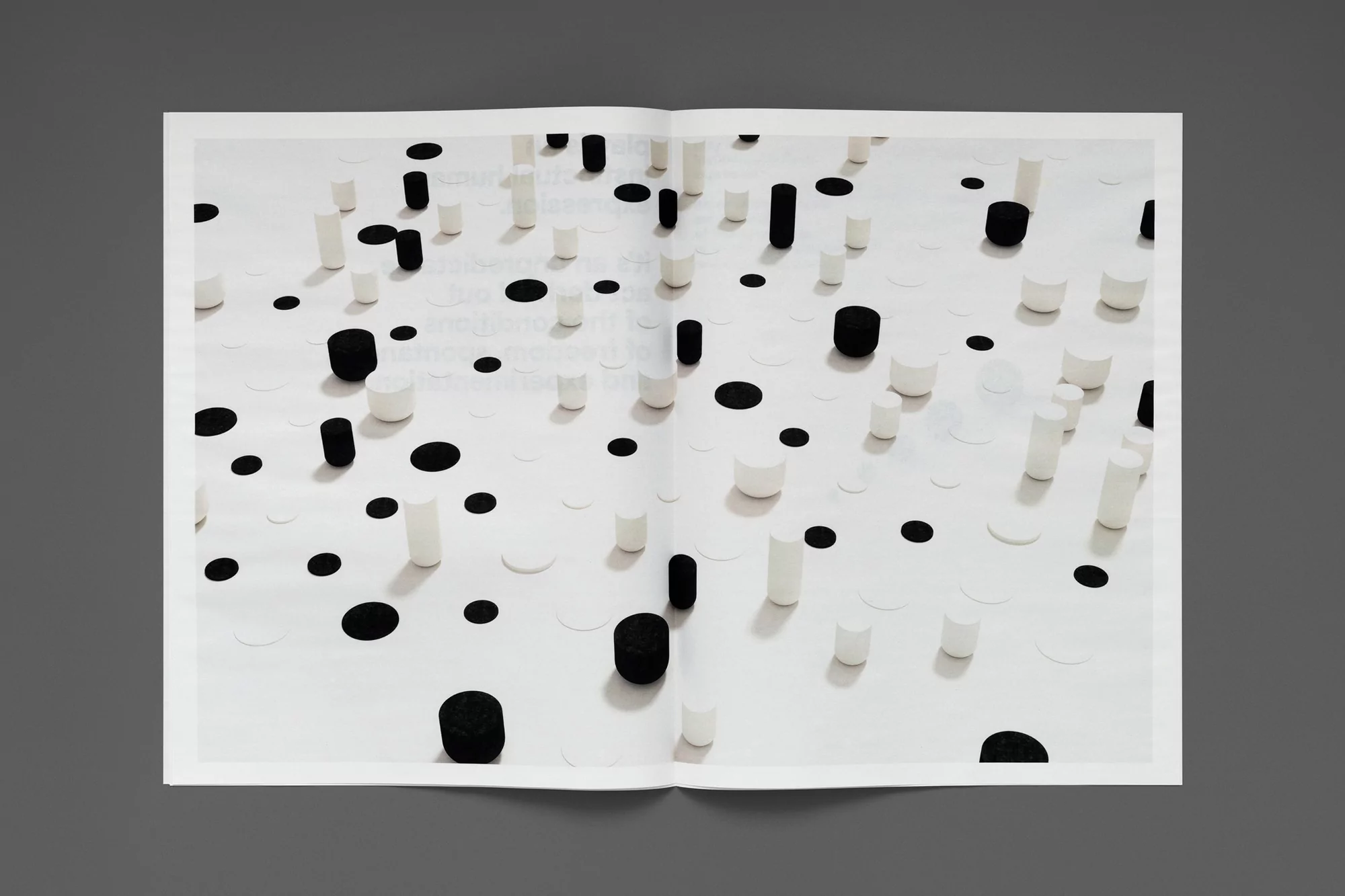 Open magazine spread featuring an abstract pattern of black and white cylinders and circles on a bright white background, gray background.