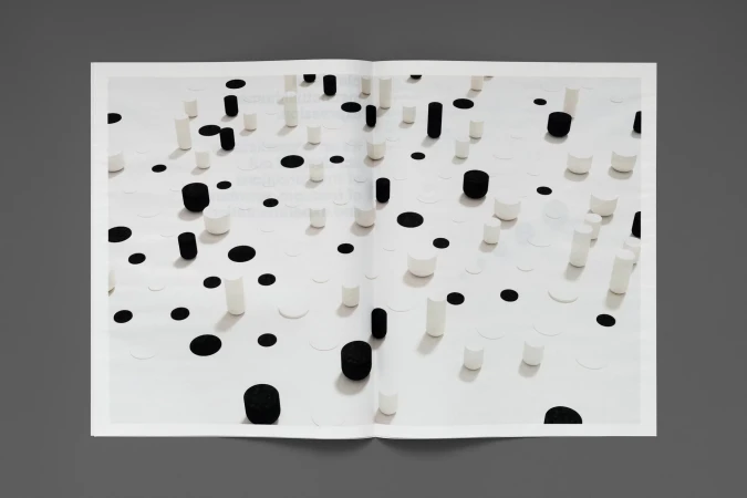 Open magazine spread featuring an abstract pattern of black and white cylinders and circles on a bright white background, gray background.