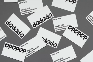 Multiple white business cards with bold black Dadada branding scattered on a grey surface.