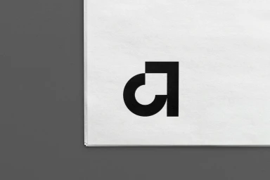 Black minimalist typographic logo design printed on white textured paper stacked on a grey surface.