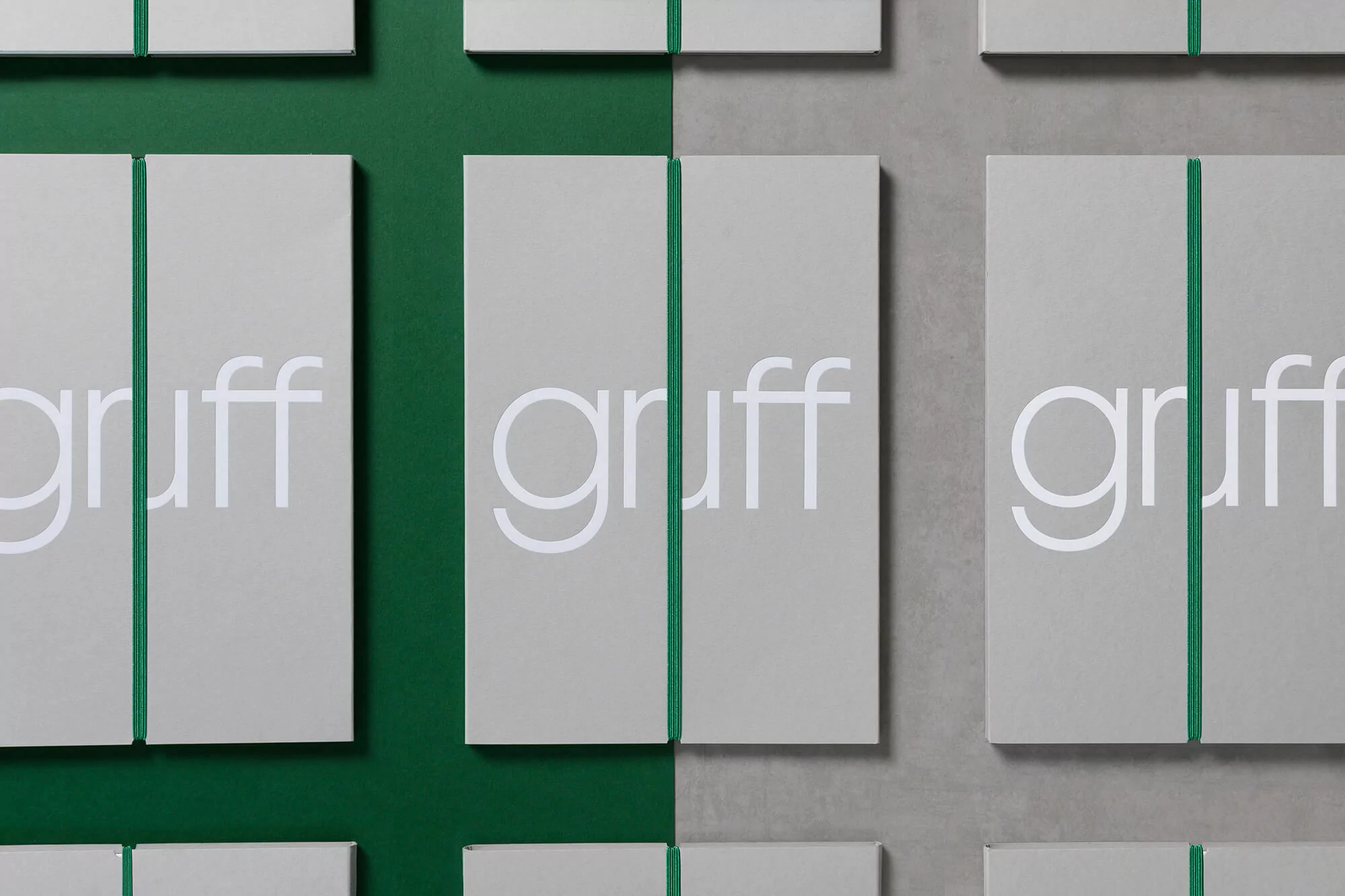Multiple 'gruff' branded notebooks with green elastic closures, arranged on a split green and gray background.
