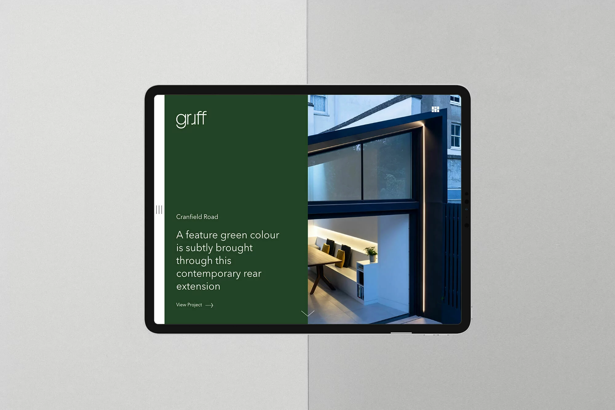 Tablet displaying modern home extension design with a green-themed website and architectural elements on screen, minimalist interior view.