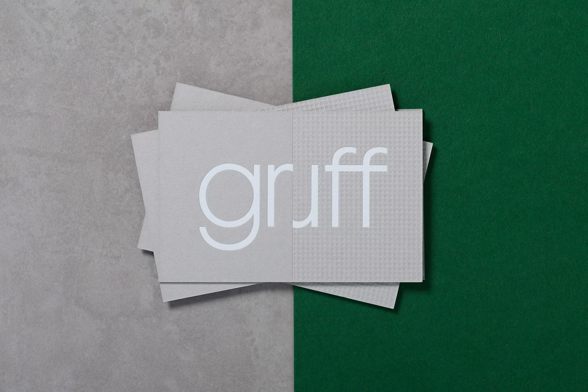 Stacked business cards with the word "gruff" in white against a grey and green background in a minimalist flat lay.
