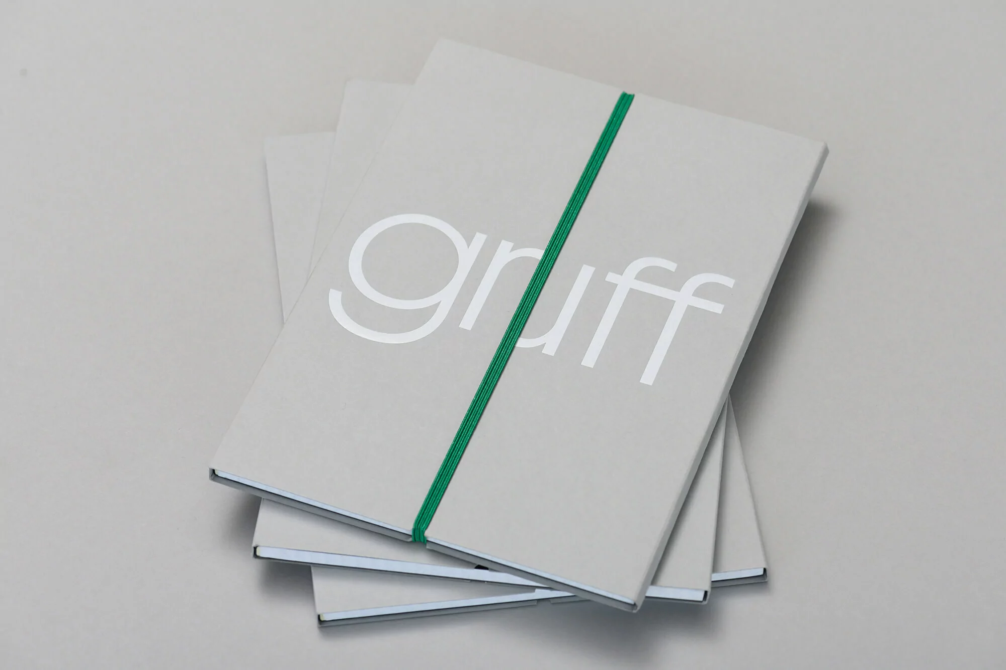 Stack of gray notebooks with the text 'gruff' in white and secured with a green elastic band, against a light gray background.
