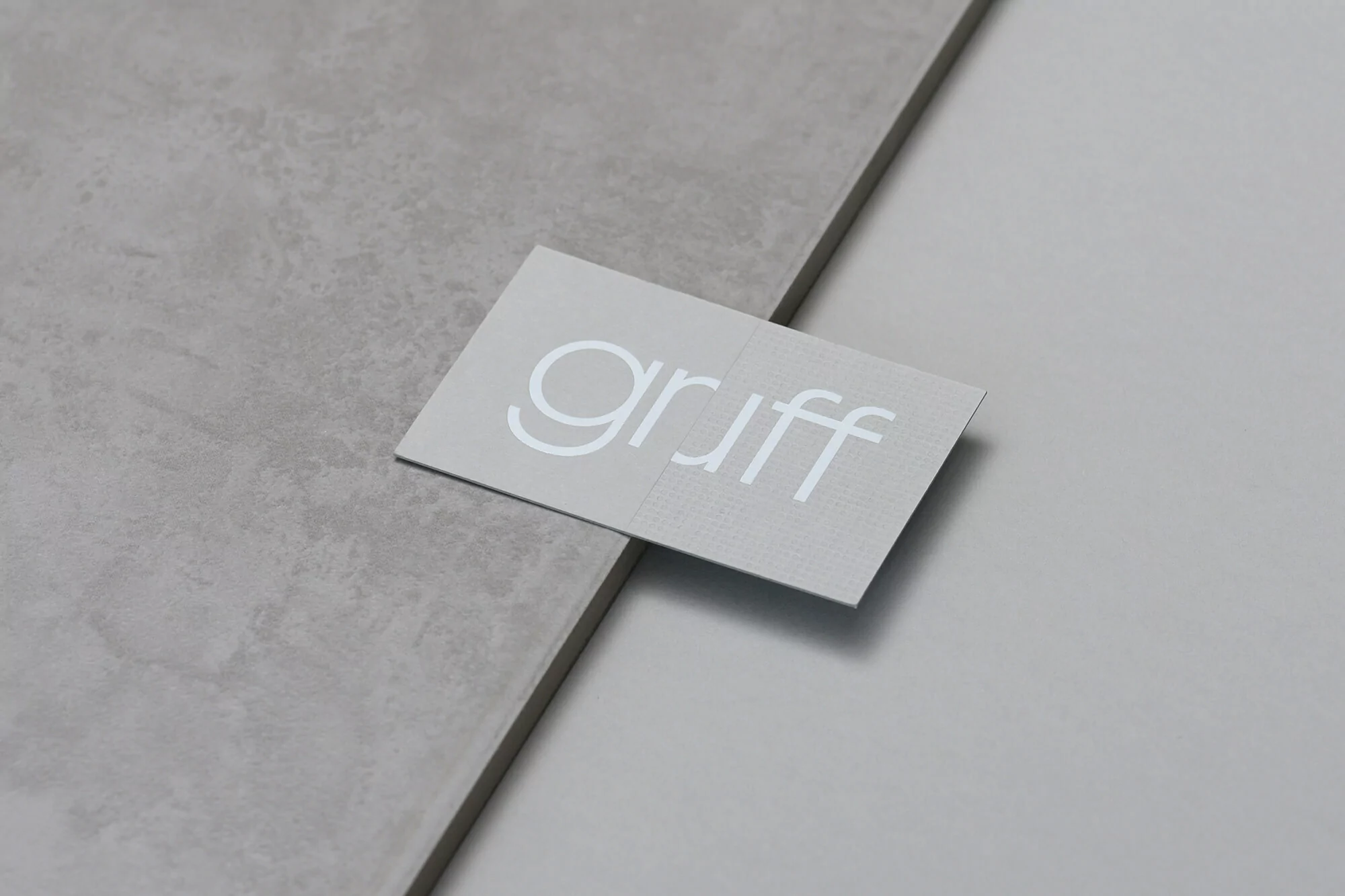Business card with the white text "gruff" rests on a light gray textured surface next to a plain light gray surface.