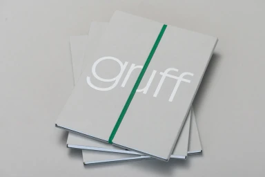 Stack of light grey notebooks with white typography and a green elastic band on a grey surface