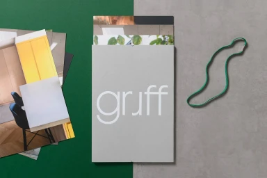 A grey brand identity folder with the text gruff on it resting on a split green and grey surface next to photographic prints and a green band