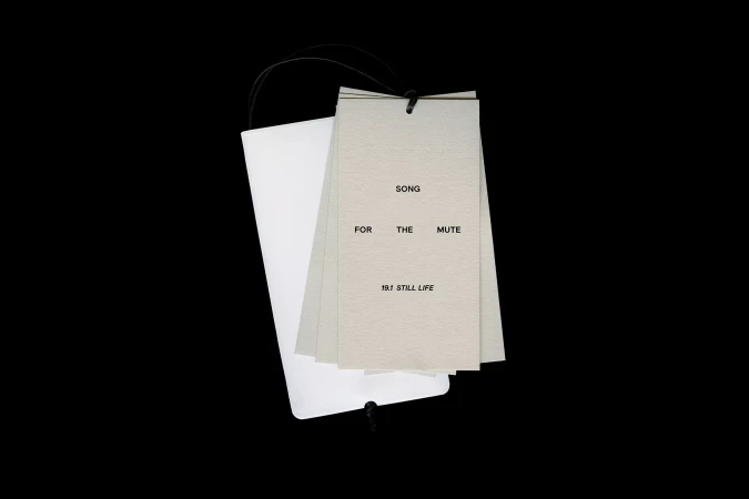 Stack of paper cards with the text 'Song For The Mute 19.1 Still Life' on a black background with black cord attached.