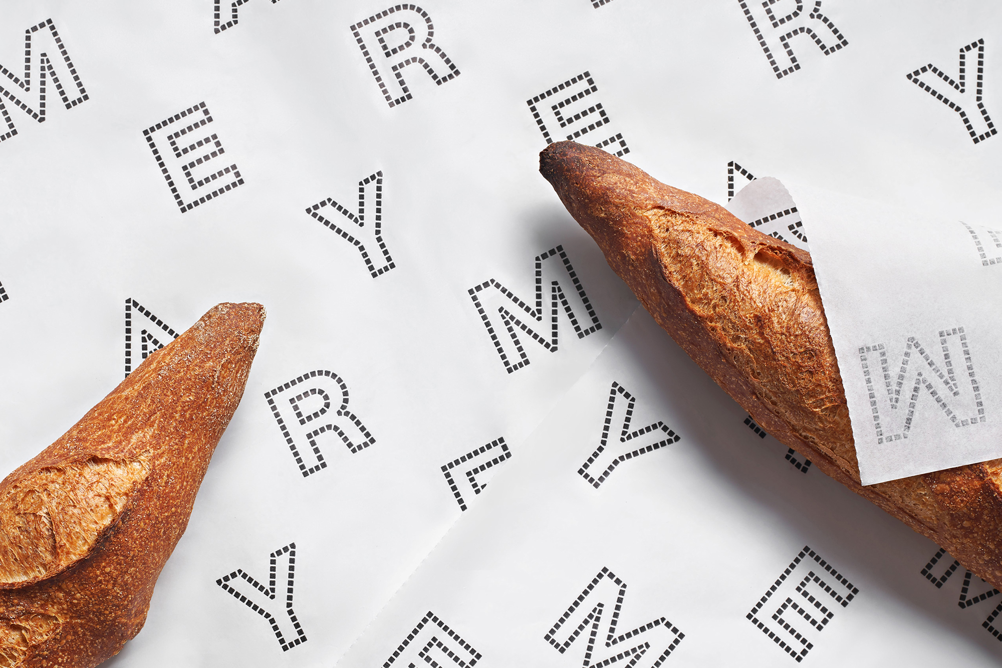 Two golden brown baguettes, one partially wrapped in white paper, are displayed on a white surface patterned with black lettering.