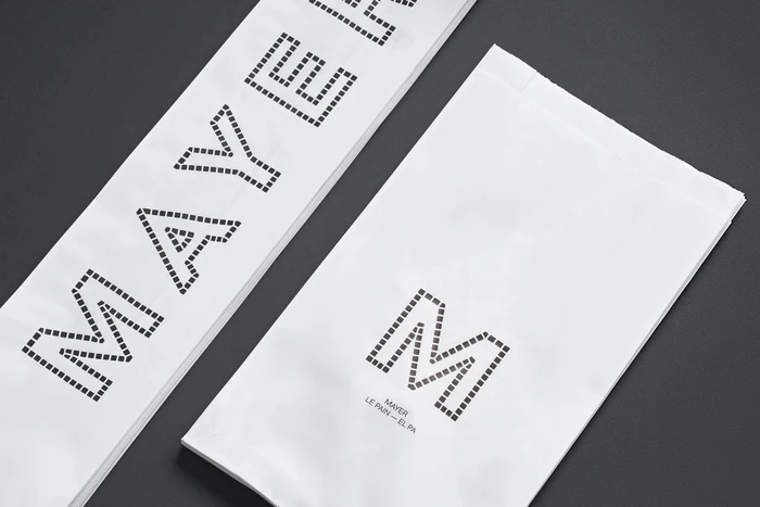 White paper bags with dotted typographic branding for Mayer displayed on a dark grey textured background.