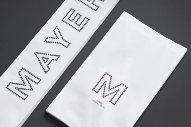 White paper bags with dotted typographic branding for Mayer displayed on a dark grey textured background.