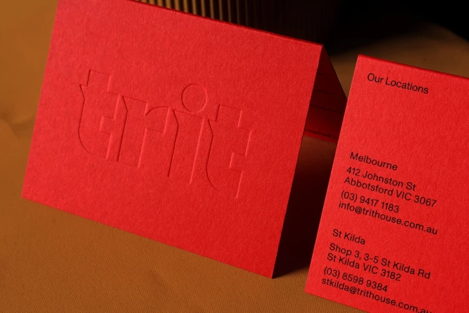 Close-up of two red business cards with embossed and printed text featuring company information and logos.