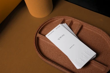 White swatch cards resting in a brown cork tray beside a ribbed yellow cylinder on a brown surface