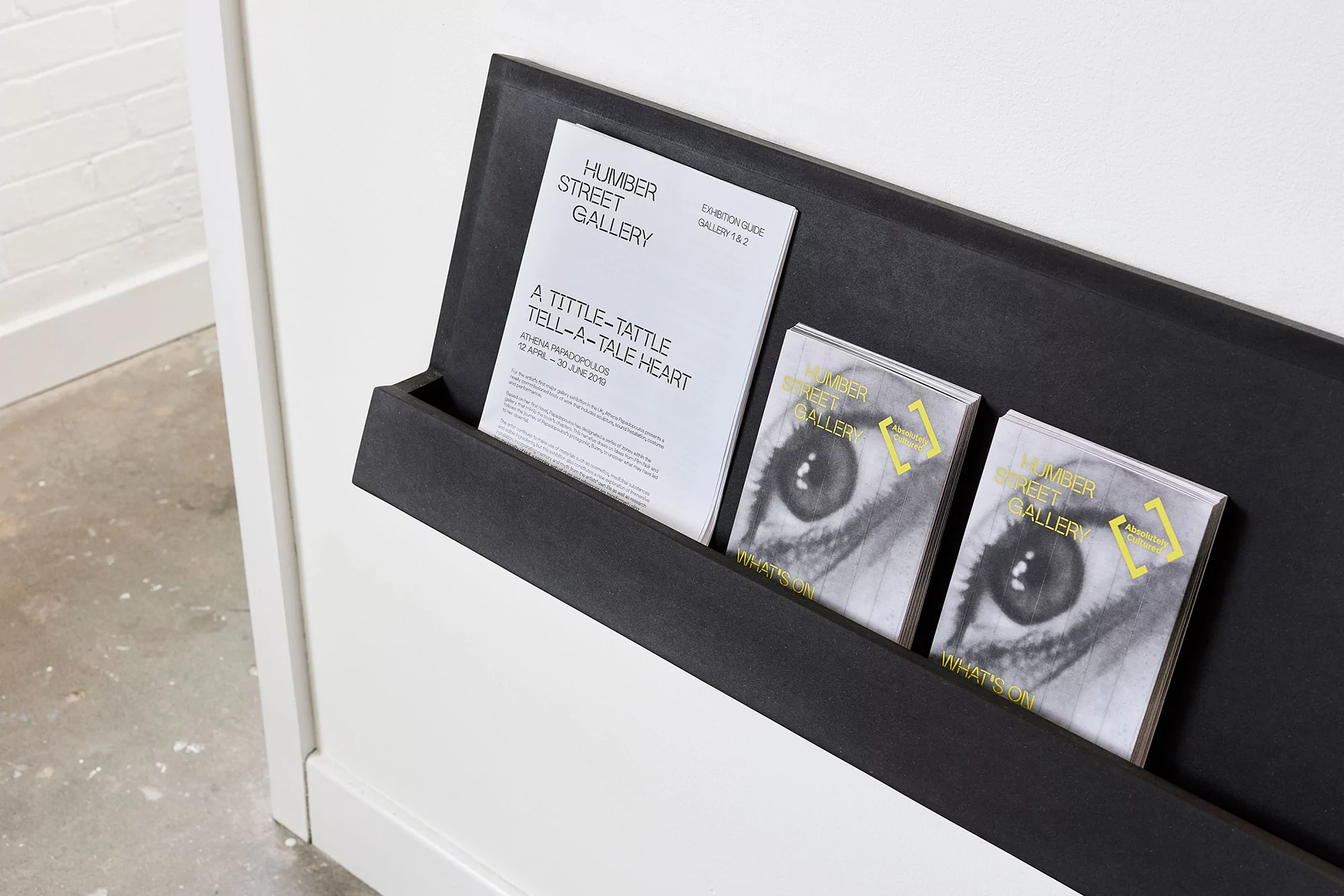 Eye-catching gallery brochures displayed on a sleek, dark-toned shelf against a clean white wall, inviting art enthusiasts.