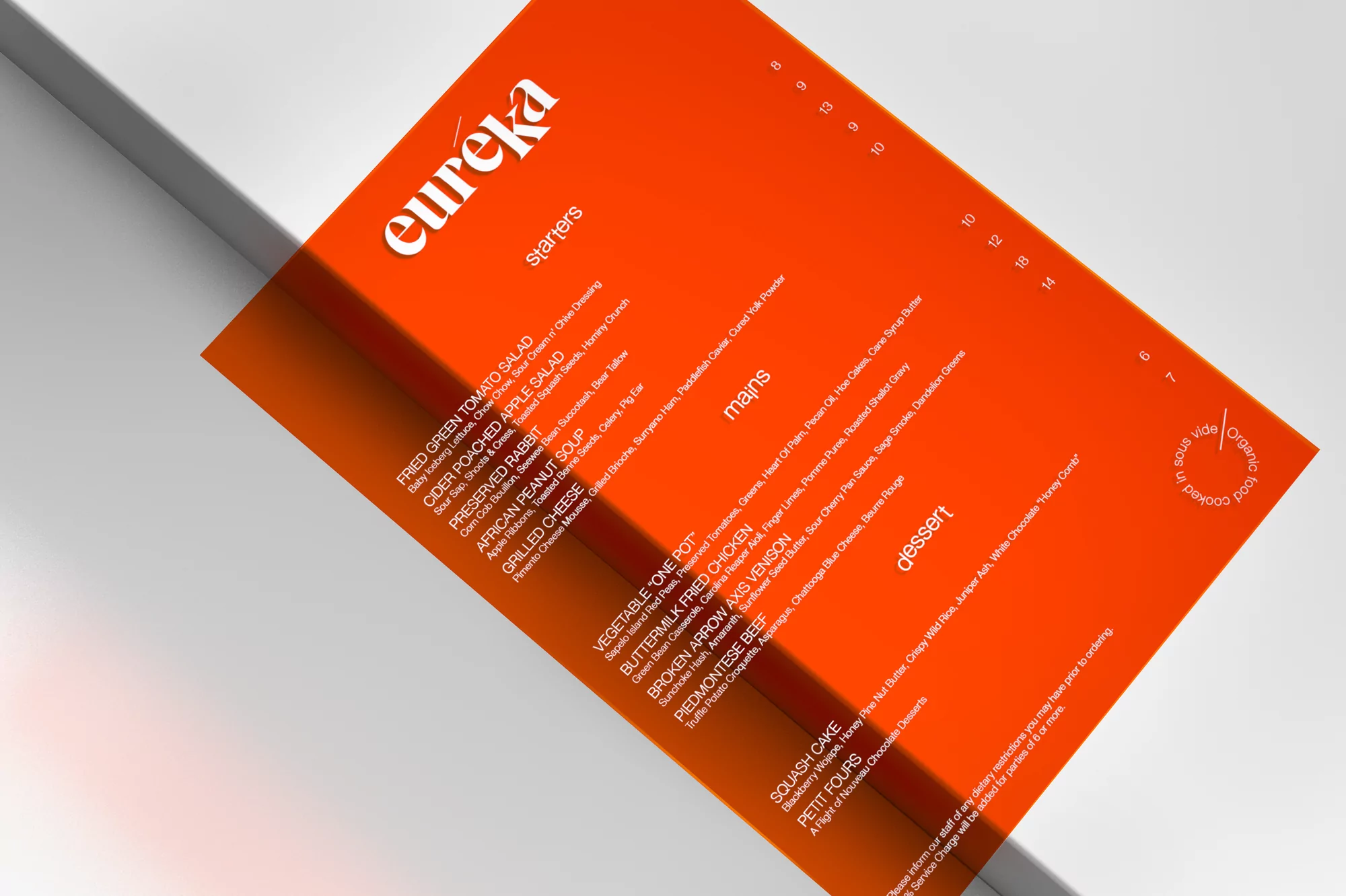 Close-up of an orange restaurant menu featuring starters, mains, and desserts, with the restaurant name 'Eureka' at the top.