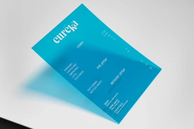 A vibrant turquoise cafe menu listing coffee, soft drinks, and alcoholic drinks, rests on a clean, white surface under bright lighting.