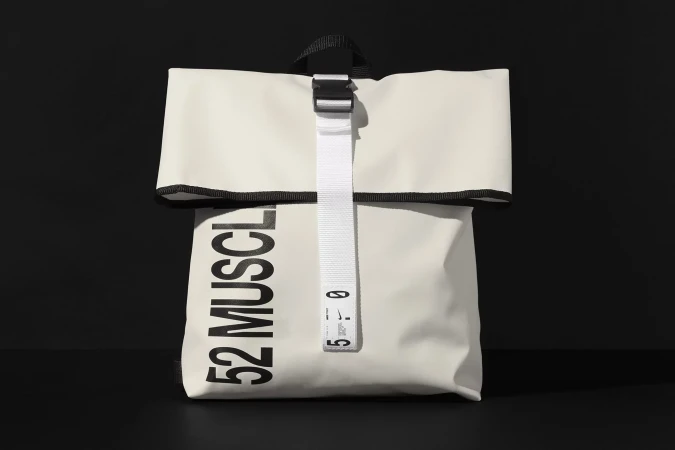 White rolltop backpack with bold black text and a white vertical strap on a black surface.