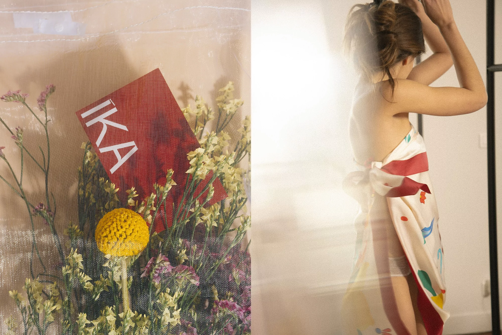 Artistic split-screen image: flowers with a red sign on the left, and a blurry, draped woman posing indoors on the right.