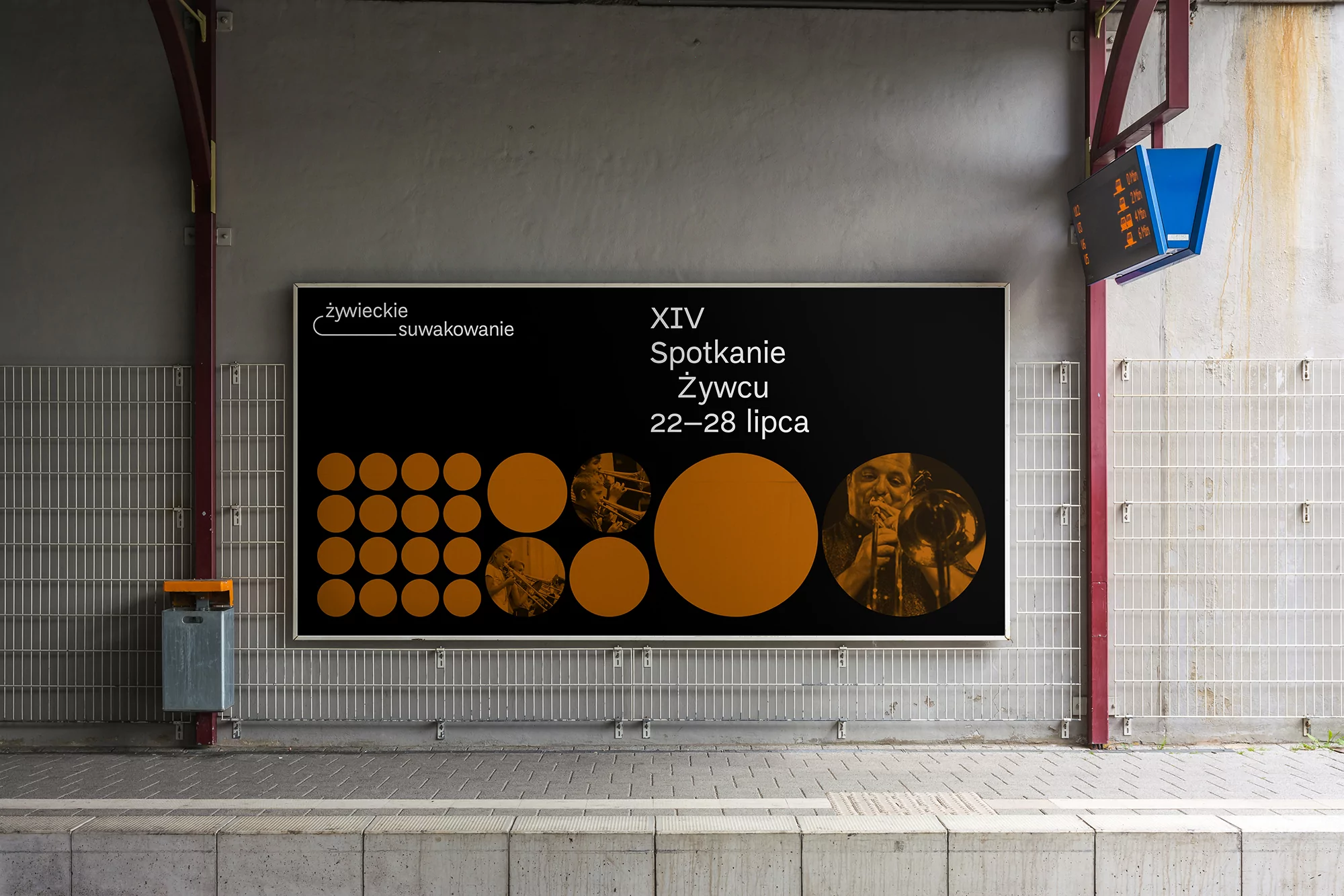 Outdoor billboard on a train platform featuring an event poster with orange circles and portraits on a black background with dates.