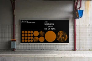Large horizontal billboard mounted on a grey concrete train station wall displaying event typography and orange circular graphic elements.