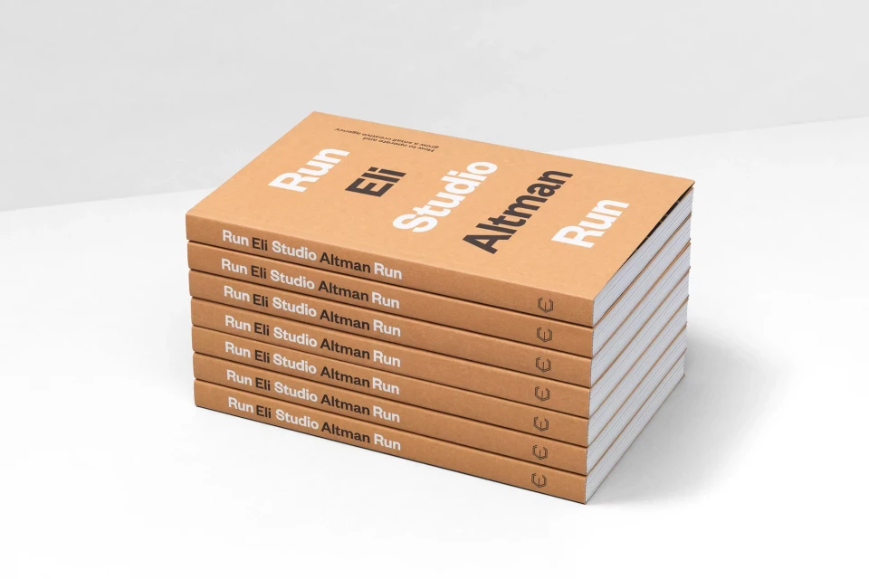 Stack of identical books with the title 'Run Eli Studio Altman Run' on a white surface and backdrop in a studio shot.