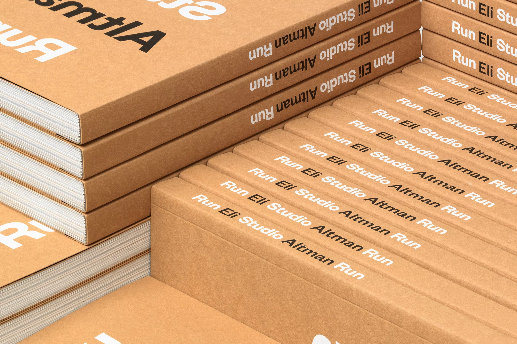 Stacks of books with kraft paper covers, featuring white text 'Run Eli Studio Altman Run' displayed in an eye-level, close-up indoor shot.