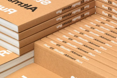 Stacked brown cardboard books with white printed typography along the spines and covers.