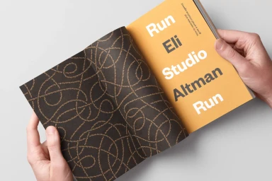 Close-up of hands holding an open book with yellow pages and a patterned dark endpaper for Eli Altman brand identity by Moniker.