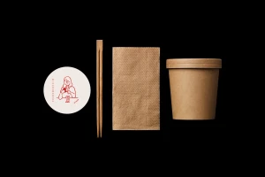 Misshumasshu brand identity flat lay featuring a round sticker, wooden chopsticks, brown napkin, and paper cup on black.