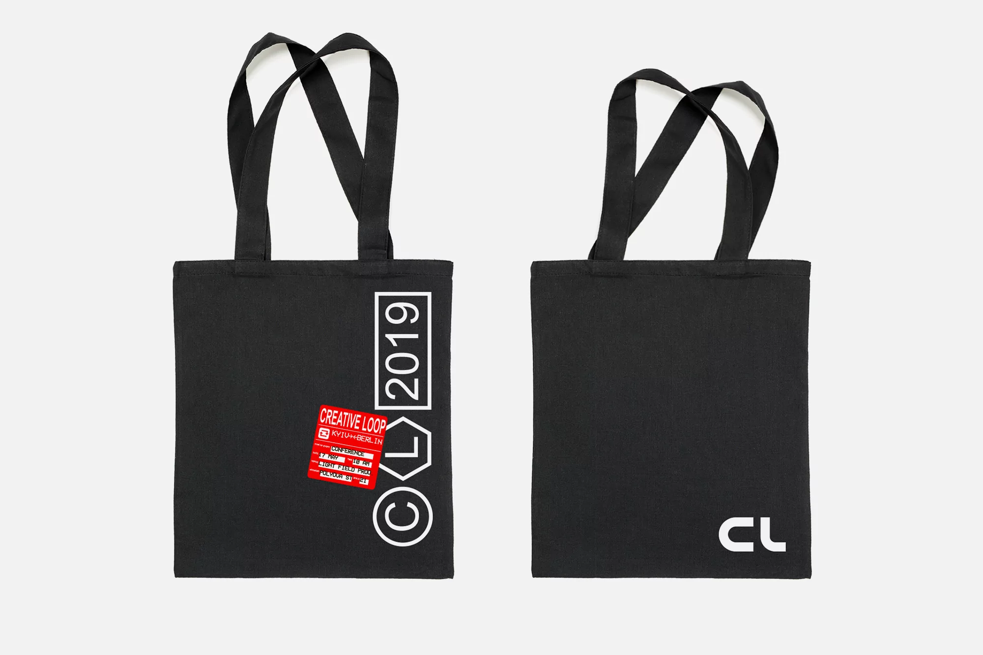 Two black tote bags displaying the 'Creative Loop 2019' logo and branding against a bright white seamless backdrop in a studio product shot.