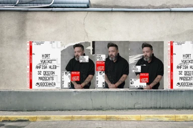 Posters pasted on a concrete urban wall featuring a bearded man in a black hoodie and graphic design typography.