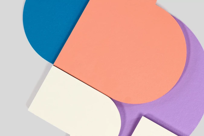 Abstract geometric shapes of blue, peach, white, and lavender create a modern, colorful composition on a gray background.