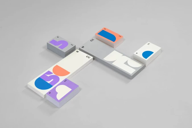 Abstract geometric designs adorn stacked business cards with 'CC' and 'W' text on a light gray background. Bold colors and shapes.