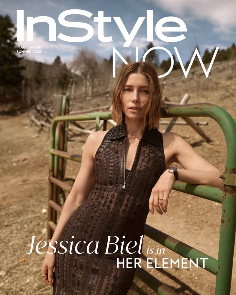 Jessica Biel gazes at the camera for InStyle magazine. She leans against a metal gate in a rural landscape with trees and sky.