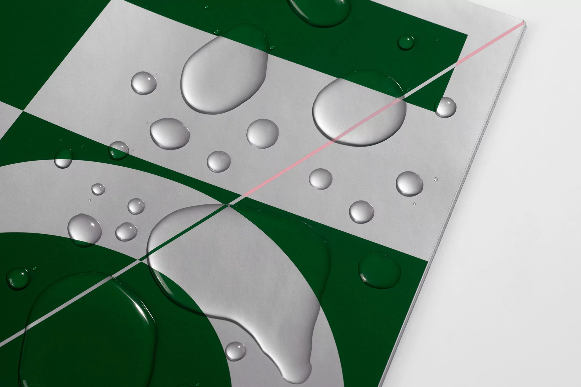 Close-up studio shot of water droplets on a glossy green and white checkered surface with geometric shapes, creating a fresh, modern aesthetic.